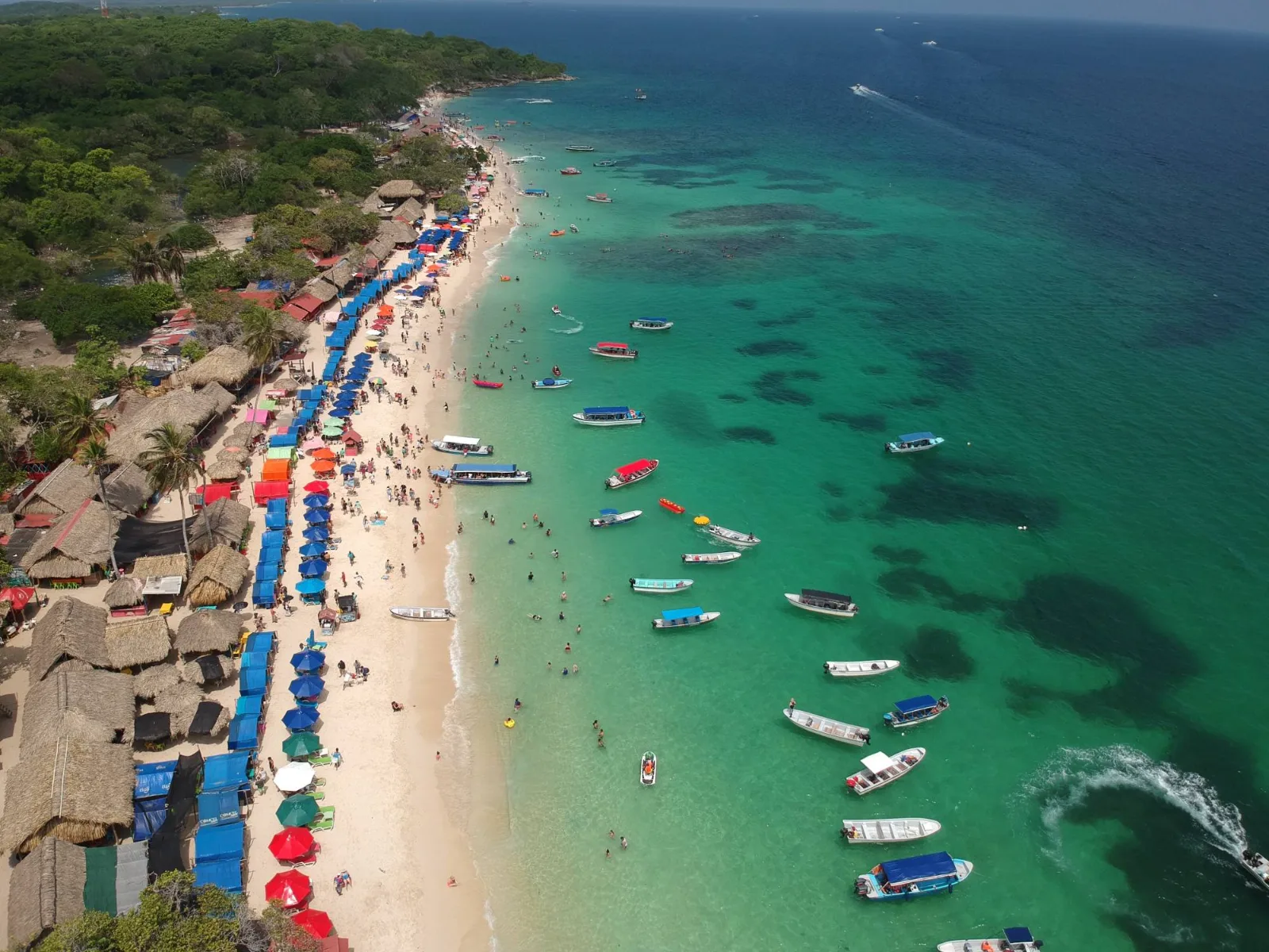 Vista aérea de Playa Blanca en Barú, Cartagena: arena blanca, kioscos, sombrillas de colores y lanchas en el agua turquesa.