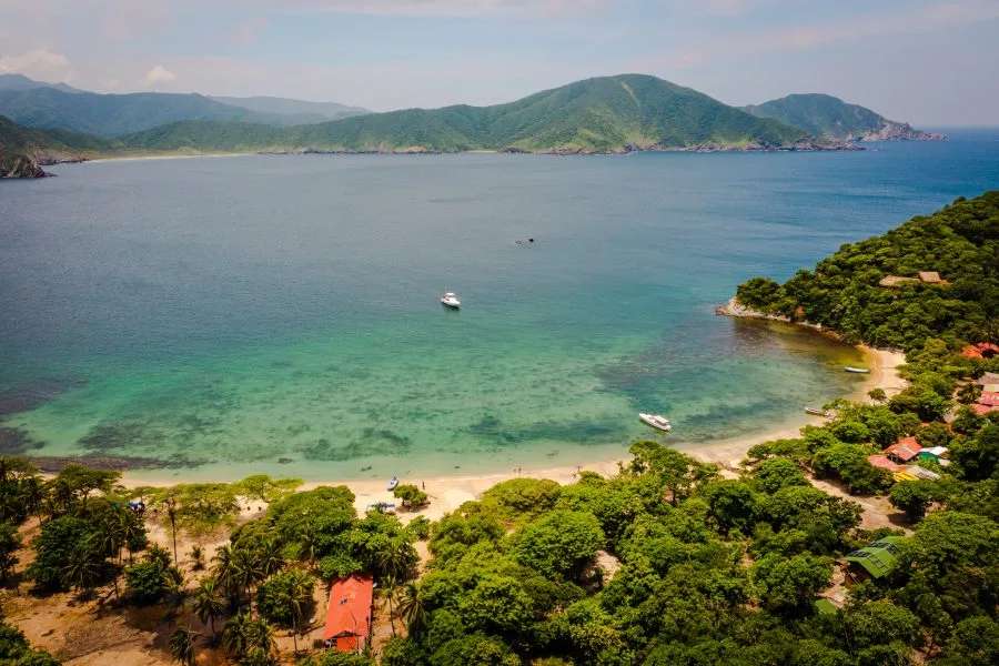 Vista aérea de Playa Cristal en el Parque Tayrona, con agua turquesa y cerros verdes.